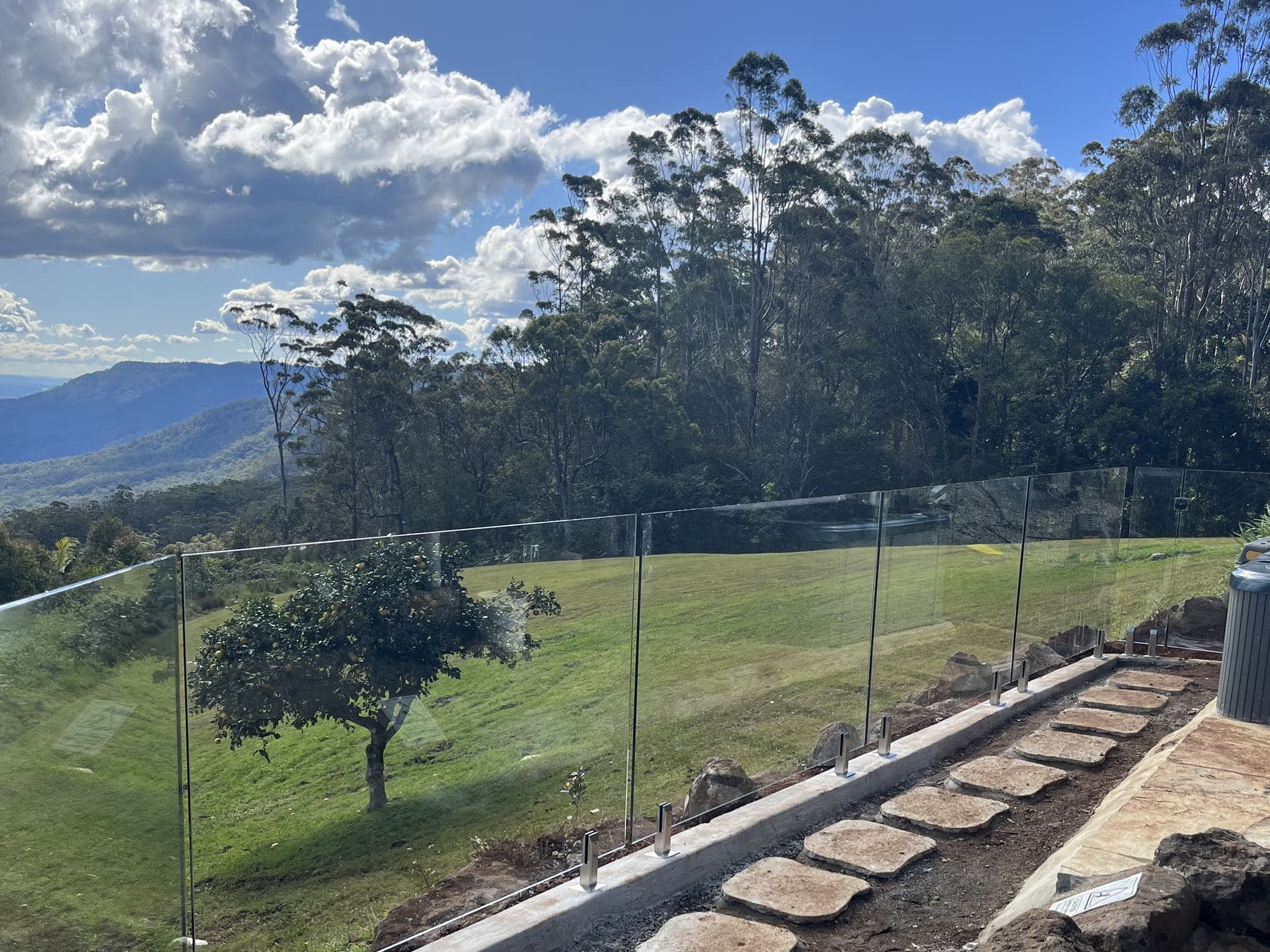 Frameless glass fencing along a hinterland acreage block with stone steps and a valley view behind