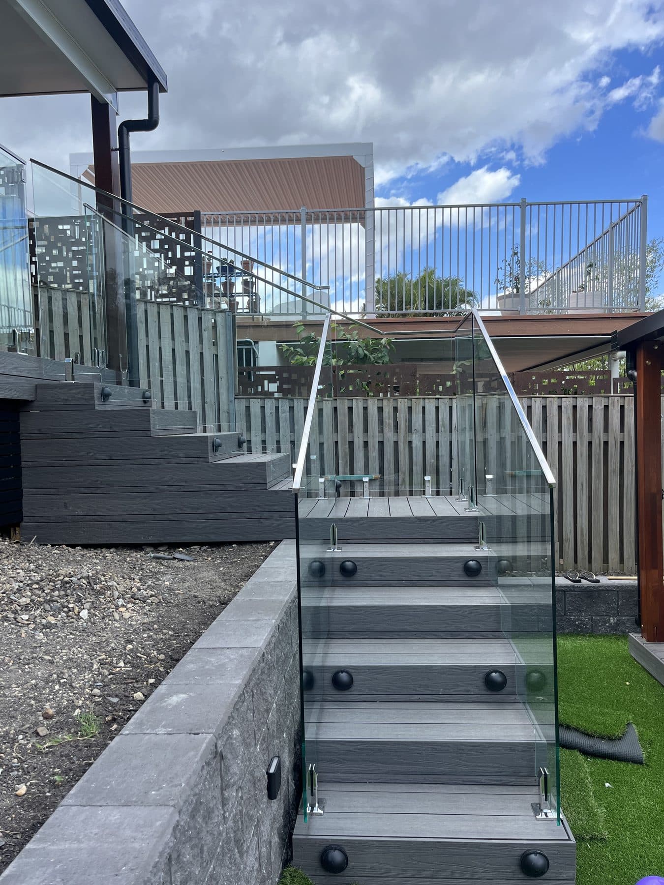 Glass balustrade on composite stairs beside a timber paling fence and a block retaining wall