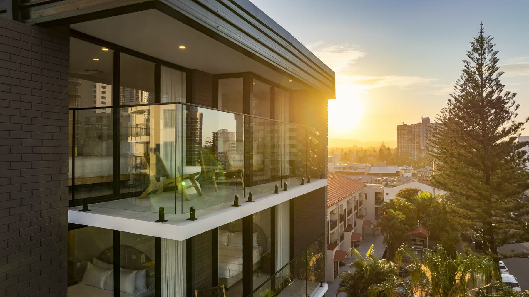 Frameless glass balustrade along an apartment balcony at sunset, above the Gold Coast rooftops