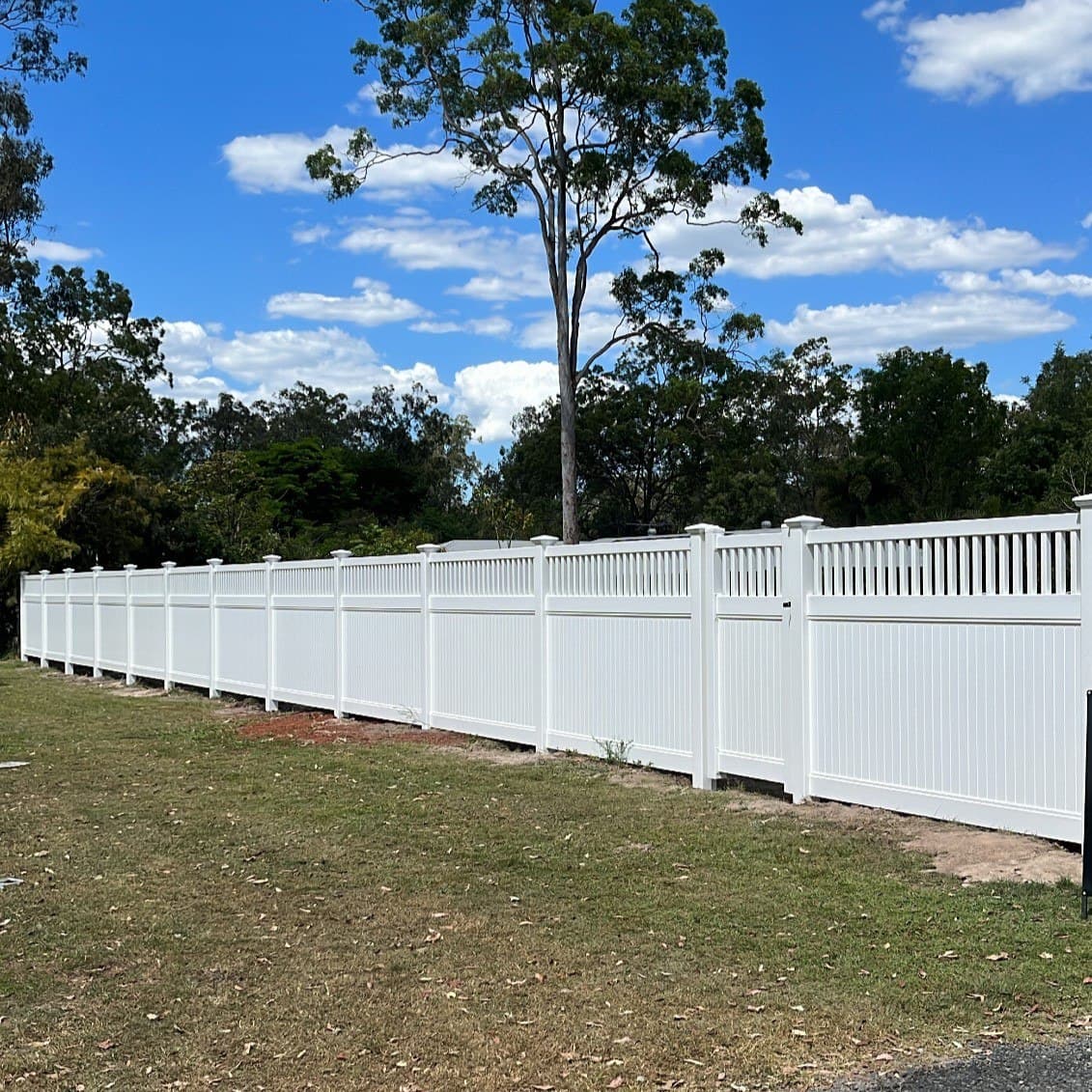 White PVC semi-privacy fence with a slatted top section running along a grassed boundary